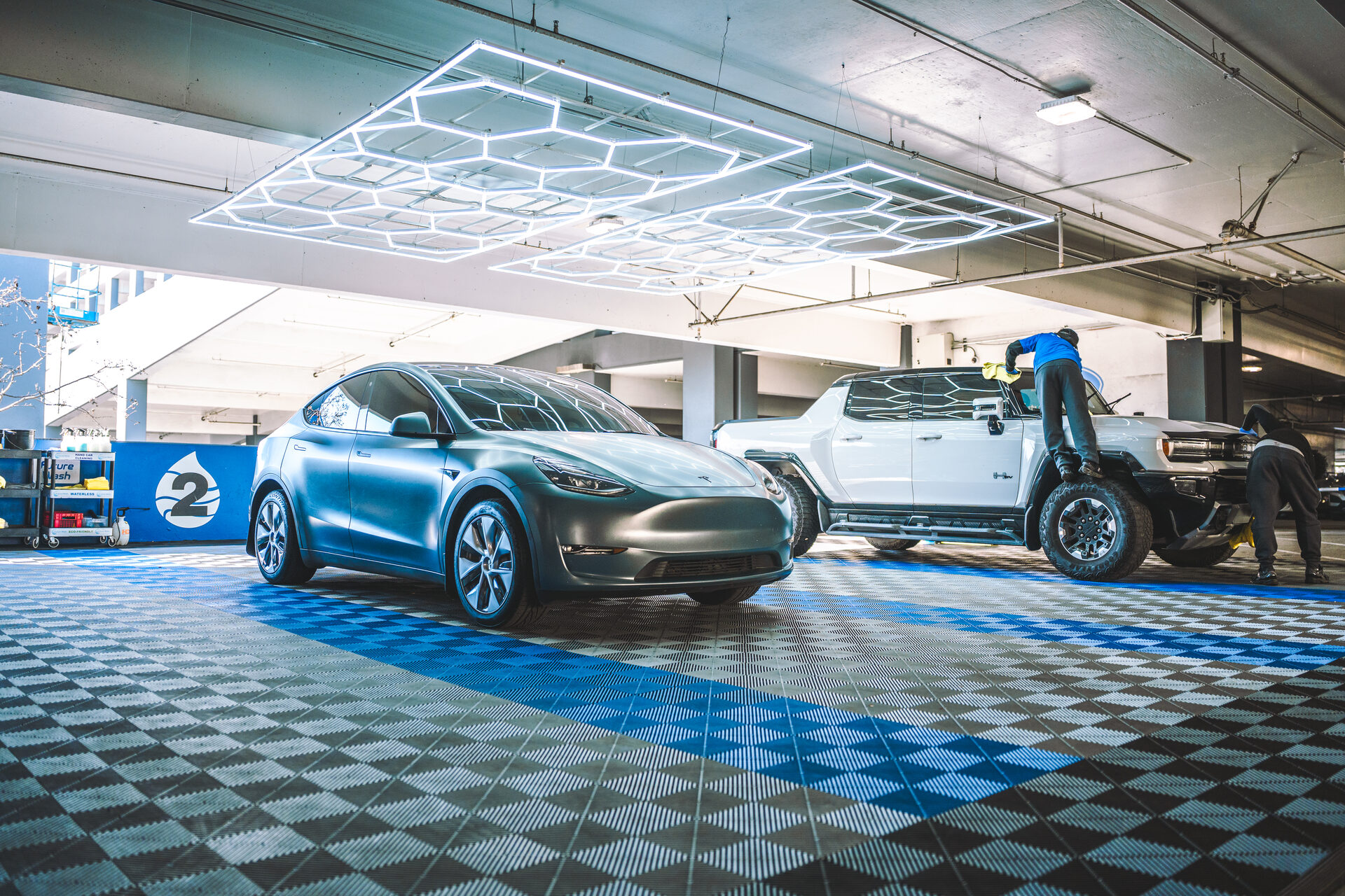 Tesla Model Y and a pickup being detailed in a Future Wash retail bay under hex LED lights